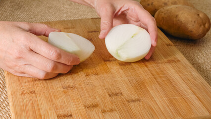 Peeling and cutting white onion on a cutting board. Vegetable soup recipe. Ingredients close-up on the kitchen table