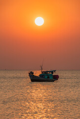 Obraz premium A scenic sunset at sea with a boat surrounded by calm waters and a fiery sky in the background. The setting sun adds a soft glow to the frame