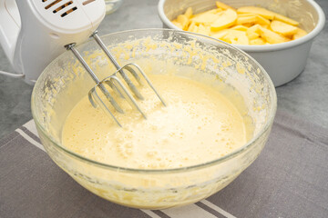 Cake batter in a glass bowl close-up on a kitchen table. Apple cake recipe