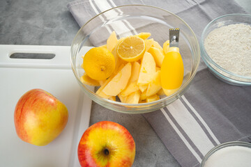 Baking pan with apple slices, lemon, eggs, sugar, and flour in bowls close-up on a kitchen table. Apple cake recipe, preparation process
