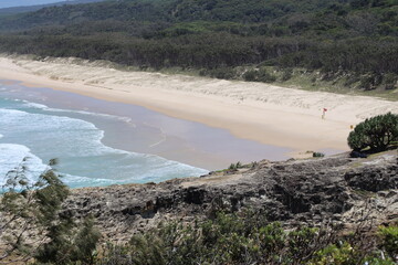 tiers of ocean waves breaking on golden sand beaches in a quiet cove viewed from rocky headlands above