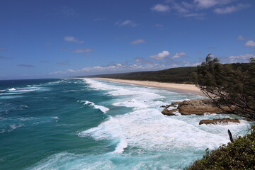 wide-angle panorama blue ocean, waves, white foam, golden sand beaches under endless blue sky skies