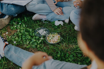 A group of students sitting together on the grass, sharing a casual picnic. Visible are takeout...