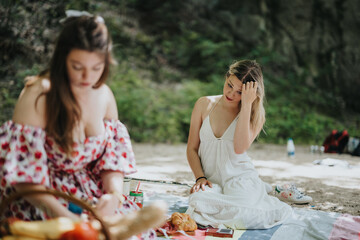 Two young women enjoying a peaceful picnic surrounded by nature. One woman in focus adjusts her hair while the other is engaged with picnic items.