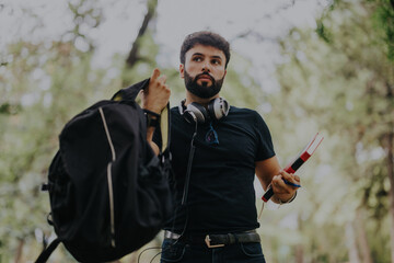 A young student in the park holding a backpack and books, engaging with classmates in a collaborative study session, highlighting teamwork and learning in a relaxed, natural environment.