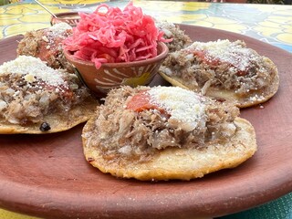 Traditional garnachas served on a clay plate at a restaurant in Oaxaca, Mexico. Deep-fried beef on masa with salsa and cheese. Close up from the side.