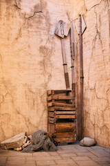 Stacked wooden planks and rustic tools leaning against an aged beige wall, reflecting traditional craftsmanship and simplicity in old Dubai architecture