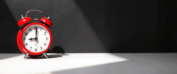 A vivid red alarm clock showcasing the time in a contrasting light and shadow environment