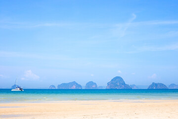 Seascape. Azure sea with boat and white sandy coast, mountains in the distance. Krabi Province Thailand.