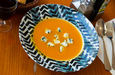 Close up of vegetarian dish, carrot cream soup with gorgonzola at plate on table