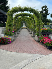 A picturesque brick-paved pathway bordered by lush flower beds in full bloom, with vibrant, colorful flowers flanking both sides.