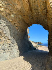 A captivating rock arch formation carved naturally over time, standing on a sandy beach under a bright blue sky.