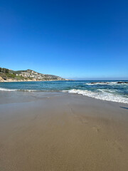 A serene view of a pristine sandy beach stretching out towards the horizon, with gentle waves caressing the shoreline under a brilliant, cloudless blue sky.
