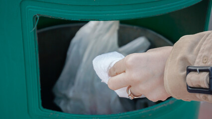 Hand throwing trash into a green bin, promoting environmental responsibility.