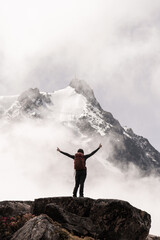 Woman with arms in a cross ascending to the snowy summit between mists and rocky landscape