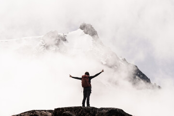 Woman with arms in a cross ascending to the snowy summit between mists and rocky landscape