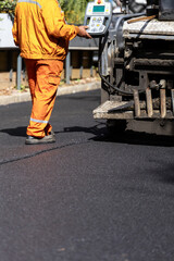 Worker operating asphalt paver on road construction site during daytime in a city setting