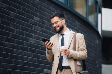 Businessman walking and using smartphone in front of brick wall