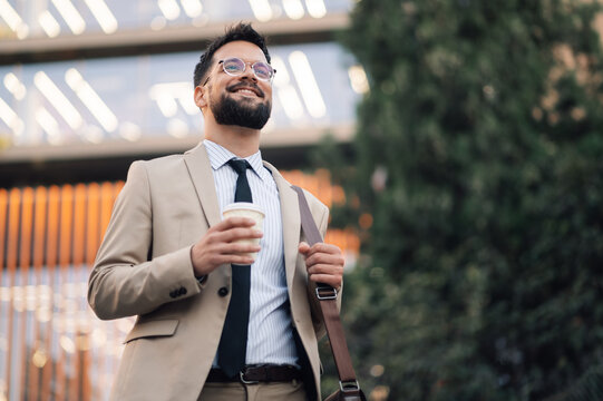 Smiling businessman holding coffee walking outside office building