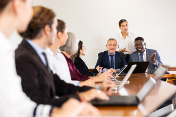 Two mid-aged male executive managers leading staff meeting and having discussion with office...