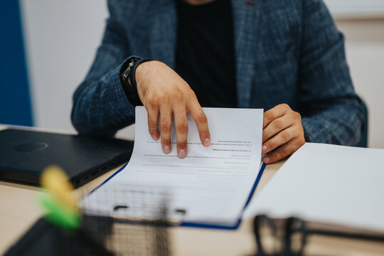A young male professor in a blazer reviews student exams at his desk, emphasizing concentration and dedication in an academic setting.