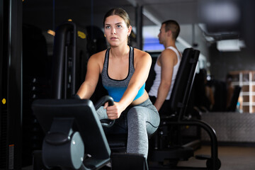 Active young woman engaged in arm workout on cable type fitness equipment in exercise room
