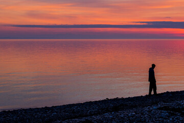 Silhouette of a man standing on a pebble beach at sunset