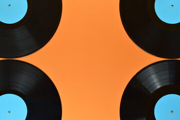 four old black vinyl records with blank cyan labels on the edges of orange background and copy space in the middle