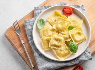 Homemade ravioli pasta with cheese, tomatoes and basil in a plate on a wooden board on a light  background