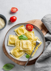 Homemade ravioli pasta with cheese, tomatoes and basil in a plate on a wooden board on a light  background