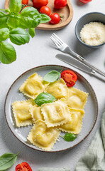 Homemade ravioli pasta with cheese, tomatoes and basil in a plate on a light  background with  fork, herb and napkin.