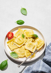 Ravioli pasta with parmesan, tomatoes and basil in a plate on a light  background with shadow and napkin.