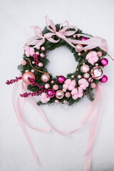 Christmas wreath made of Christmas tree branches, decorated with pink balls lies on a round table covered with white snow