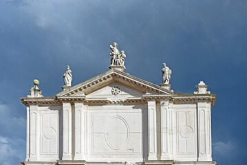 Top gable with tympanum and sculptures of the baroque San Toma church in Venice on a clouded summer day