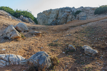 A sunlit pathway winding through rugged terrain on a quiet morning at the rocky hillside.