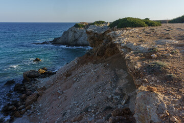 A coastal view of eroded cliffs meeting the serene blue sea during a tranquil afternoon.