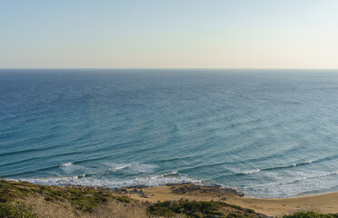 Waves gently lapping against the golden shore under a serene, sunlit sky near a tranquil coastline.