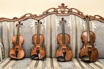 three different violins and a viola on an antique couch