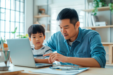 Obraz premium Asian father assisting his young son with a laptop in a bright, homey setting, fostering learning or bonding through technology