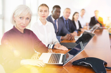 Senior businesswoman using laptop during conference in meeting room. Woman sitting at desk with colleaugues.