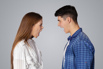Breakup of relations, quarrel, problems in couple and scandal. Angry aggressive young man and lady yelling at each other with open mouths, isolated on gray background, studio shot, profile, free space