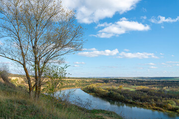 A serene river flows gently beneath a blue sky in late afternoon