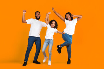 Having Fun. Full body length of excited young black family of three dancing and fooling around. Happy African American man, woman and girl enjoying favorite music together on yellow studio background