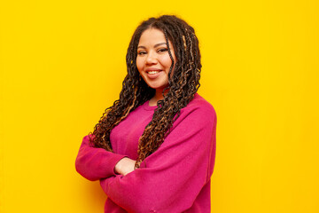 plump african american woman with dreadlocks smiling with arms crossed on yellow background, big plus size girl with pigtails looking at camera