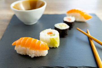 Assorted sushi set, salmon nigiri, avocado makis and california roll on slate plate with chopsticks and soy bowl photographed from the front on a gourmet restaurant table. Japanese food.