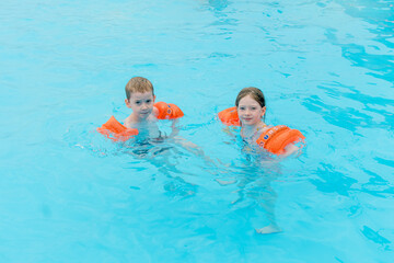 children are swimming in a pool wearing orange armbands.