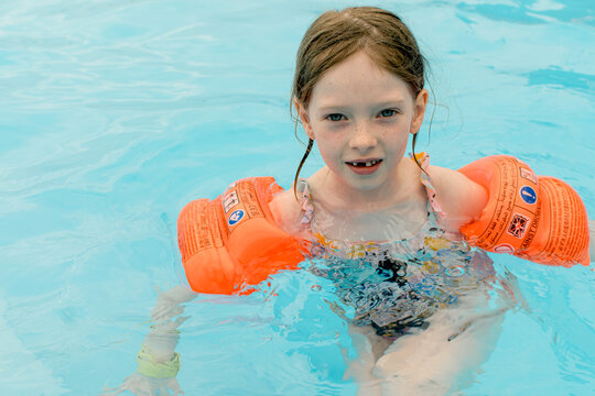 Happy girl are swimming in a pool wearing orange armbands.