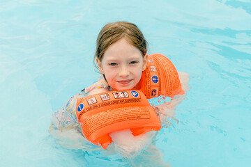 Happy girl are swimming in a pool wearing orange armbands.