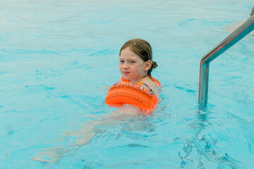 Happy girl are swimming in a pool wearing orange armbands.