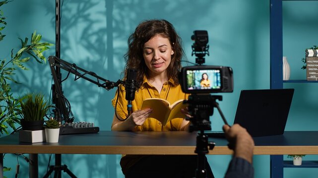Excited content creator films video review of book, browsing through pages, impressed by story. Online star giving her impressions of new novel release to readers, giving positive feedback, camera A